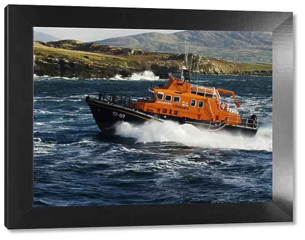 Valentia severn class lifeboat John and Margaret Doig 17-07. Lifeboat is moving from right to left in choppy seas, lots of white spray and waves breaking against rocks in the background