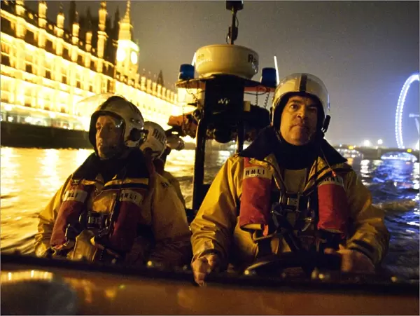 Tower lifeboat crew members on board an E-class lifeboat on the River Thames at night, Houses of Parliament and the London Eye in the background