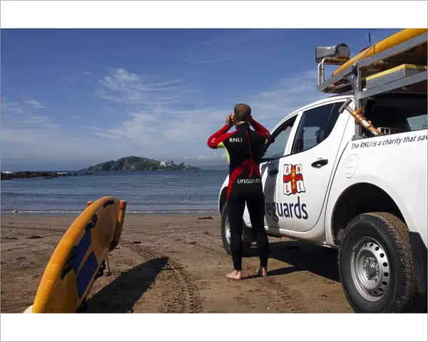 A lifeguard on Bantham beach monitoring the sea through a pair of binoculars. The lifeguard is stood next to a 4x4 patrol vehicle and yellow rescue board