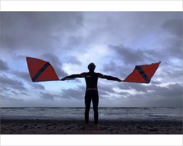 Lifeguard on Cromer beach waving two red flags. Silhouette