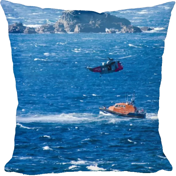 Relief fleet Tamar class lifeboat Peter & Lesley Jane Nicholson 16-01 ON 1280. Portrait shot showing the lifeboat in choppy seas, a helicopter above and Longships lighthouse near Sennen Cove in the background