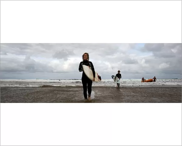 Two surfers walking in from the sea towards the camera, two lifeguards and an arancia in the background. Used as the RNLI You Tube banner