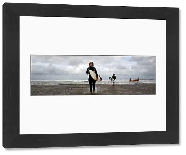 Two surfers walking in from the sea towards the camera, two lifeguards and an arancia in the background. Used as the RNLI You Tube banner