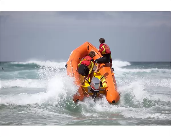 Two RNLI lifeguards heading through a breaking wave on an arancia inshore rescue boat, bow high out of the water