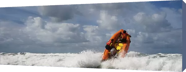 Two RNLI lifeguards heading over a breaking wave at Woolacombe beach, Devon on an arancia inshore rescue boat, bow high out of the water