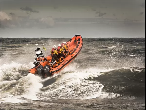 Sheringham Atlantic 85 inshore lifeboat The oddfellows B-818. Lifeboat is heading away from the camera over a breaking wave, bow high out of the water and four crew on board