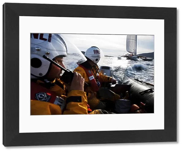 Two crew members from Barra RNLI on an ILB in the foreground, one talking into a radio. Yacht competing in the Round Britain and Ireland yacht race 2010 in the background. Leisure