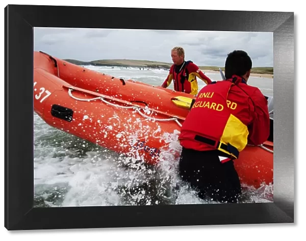 Two lifeguards launching an arancia inshore rescue boat at Constantine Bay, Cornwall