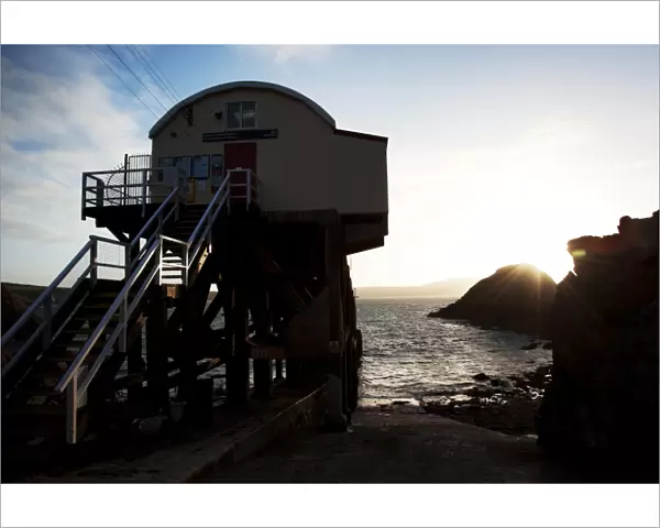 St Davids lifeboat station. Shot from behind the station looking out to sea, sun setting behind rocks in the distance