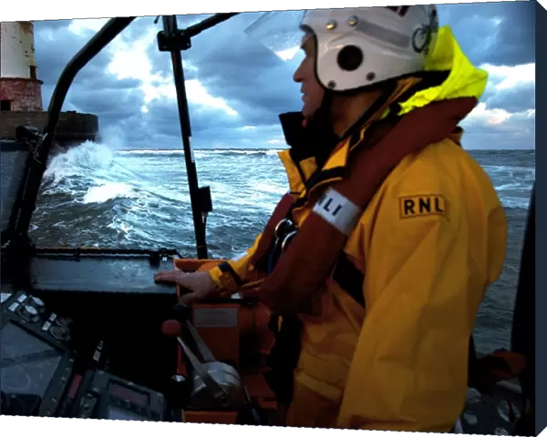 Coxswain stood at the helm of the Berwick-upon-Tweed Mersey class lifeboat Joy and Charles Beeby 12-32, lots of spray, lighthouse in the background