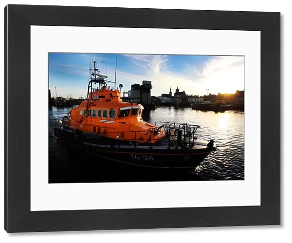 Fraserburgh Trent class lifeboat Willie and Mary Gall 14-34 in the harbour, sun low behind buildings in the background