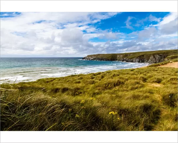 Landscape shot of Holywell beach, Cornwall. People in the sea swimming and surfing, lifeguards on an arancia inshore rescue boat in the distance by the cliffs