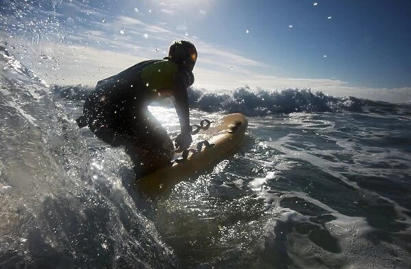Female lifeguard paddling out through surf on a rescue board at Constantine Bay, Cornwall