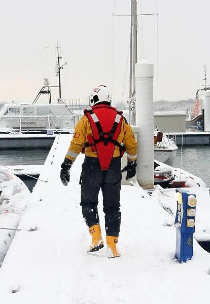Lifeboat crew member walking along a snow covered pontoon at the Lifeboat College, Poole