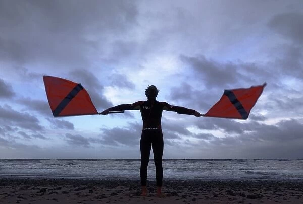 Lifeguard on Cromer beach waving two red flags. Silhouette