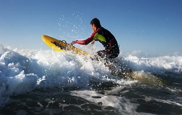 Lifeguard paddling out through surf on a rescue board at Constantine Bay, Cornwall