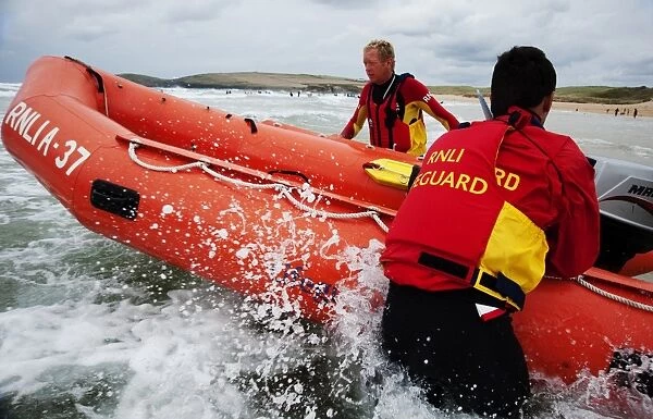 Two lifeguards launching an arancia inshore rescue boat at Constantine Bay, Cornwall