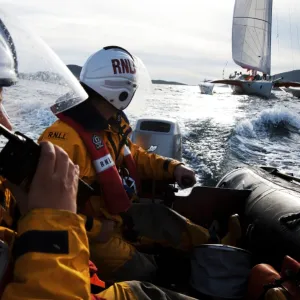 Two crew members from Barra RNLI on an ILB in the foreground, one talking into a radio. Yacht competing in the Round Britain and Ireland yacht race 2010 in the background. Leisure