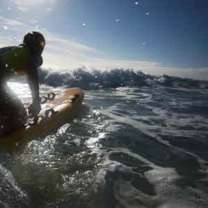 Female lifeguard paddling out through surf on a rescue board at Constantine Bay, Cornwall