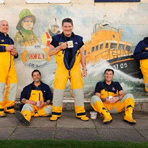 Group shot of Humber crew members lounging against a wall with lifeboat mural on and drinking cups of tea