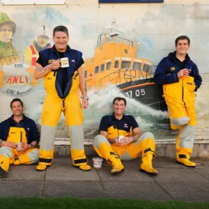 Group shot of Humber crew members lounging against a wall with lifeboat mural on and drinking cups of tea