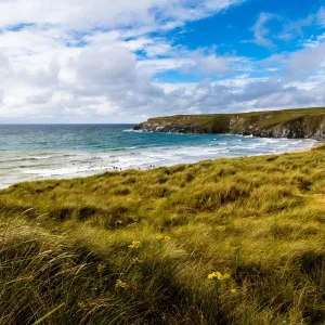 Landscape shot of Holywell beach, Cornwall. People in the sea swimming and surfing, lifeguards on an arancia inshore rescue boat in the distance by the cliffs