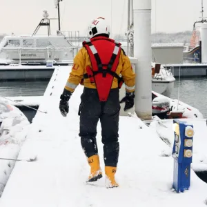 Lifeboat crew member walking along a snow covered pontoon at the Lifeboat College, Poole