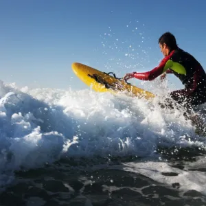 Lifeguard paddling out through surf on a rescue board at Constantine Bay, Cornwall