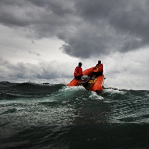 Two lifeguards on an arancia inshore rescue boat at Watergate Bay, Cornwall, headingaway from the camera