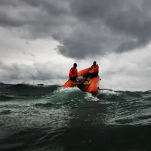 Two lifeguards on an arancia inshore rescue boat at Watergate Bay, Cornwall, headingaway from the camera