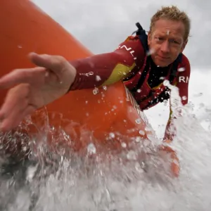 Two lifeguards on an arancia inshore rescue boat at Watergate Bay, Cornwall, heading towards the camera. Lifeguard reaching down towards casualty