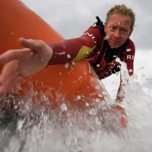 Two lifeguards on an arancia inshore rescue boat at Watergate Bay, Cornwall, heading towards the camera. Lifeguard reaching down towards casualty Two lifeguards on an arancia inshore rescue boat at Watergate Bay, Cornwall, heading towards the camera. Lifeguard reaching down towards casualty