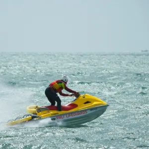 RNLI lifeguard on a rescue watercraft off Sandbanks beach, Poole. Moving from left to right at speed, Old Harry Rocks in the distance