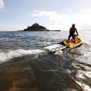 RNLI lifeguard on a rescue watercraft (RWC) with St Michaels Mount near Penzance in the background