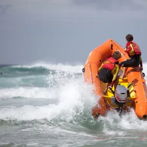 Two RNLI lifeguards heading through a breaking wave on an arancia inshore rescue boat, bow high out of the water