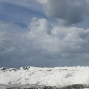 Two RNLI lifeguards heading over a breaking wave at Woolacombe beach, Devon on an arancia inshore rescue boat, bow high out of the water