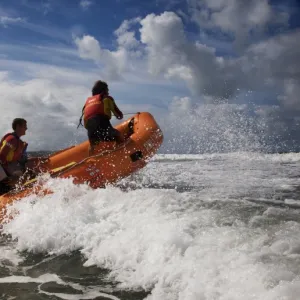 Two RNLI lifeguards in the surf at Woolacombe beach, Devon on an arancia inshore rescue boat