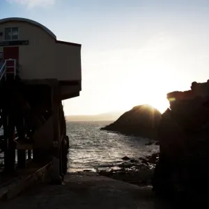St Davids lifeboat station. Shot from behind the station looking out to sea, sun setting behind rocks in the distance St Davids lifeboat station. Shot from behind the station looking out to sea, sun setting behind rocks in the distance