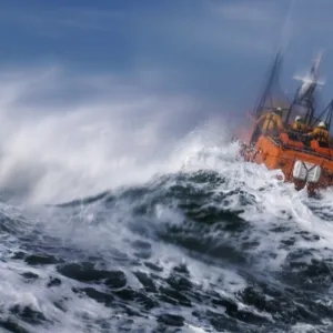 St Davids Tyne class lifeboat Garside 47-026 in rough seas. Three crew can be seen at the upper steering position. Lifeboat is partially obscured by a large wave and lots of white water