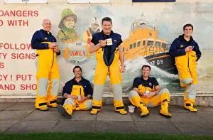 Group shot of Humber crew members lounging against a wall with lifeboat mural on and drinking cups of tea