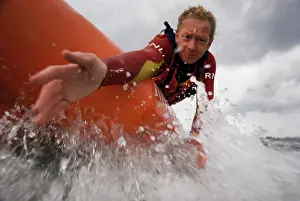 Two lifeguards on an arancia inshore rescue boat at Watergate Bay, Cornwall, heading towards the camera. Lifeguard reaching down towards casualty