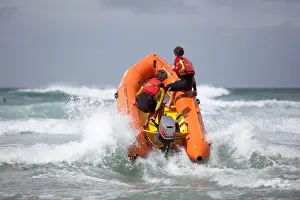 Two RNLI lifeguards heading through a breaking wave on an arancia inshore rescue boat, bow high out of the water