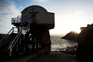 St Davids lifeboat station. Shot from behind the station looking out to sea, sun setting behind rocks in the distance