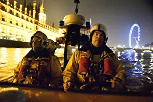 Tower lifeboat crew members on board an E-class lifeboat on the River Thames at night, Houses of Parliament and the London Eye in the background
