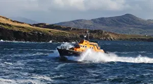 Valentia severn class lifeboat John and Margaret Doig 17-07. Lifeboat is moving from right to left in choppy seas, lots of white spray and waves breaking against cliffs in the background